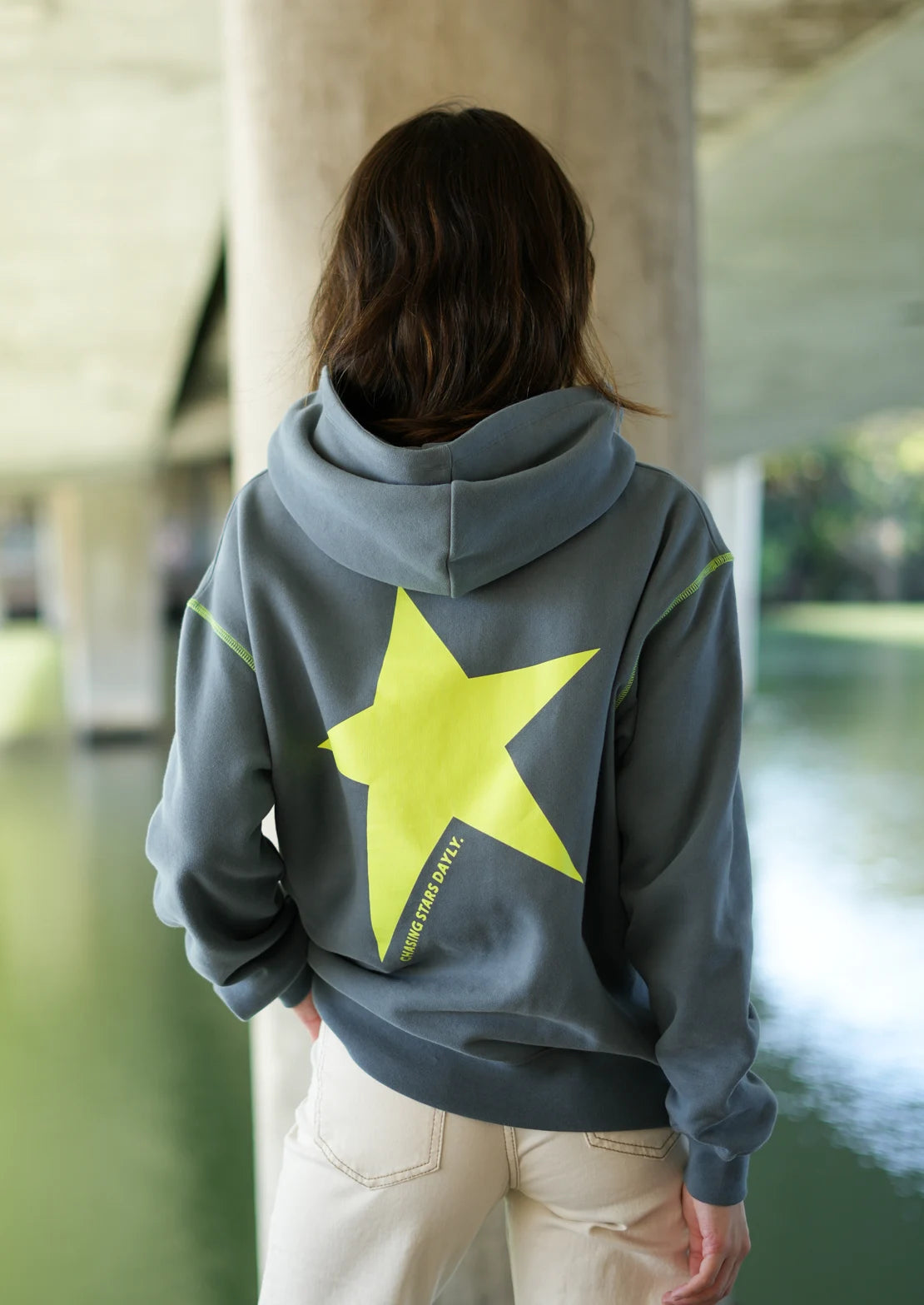 Sudadera ideal para teens en gris, con capucha y bolsillo canguro de To the Moon. SerigrafĂa trasera amarillo flĂșor con estrella y frase "Chasing Stars Daily".
