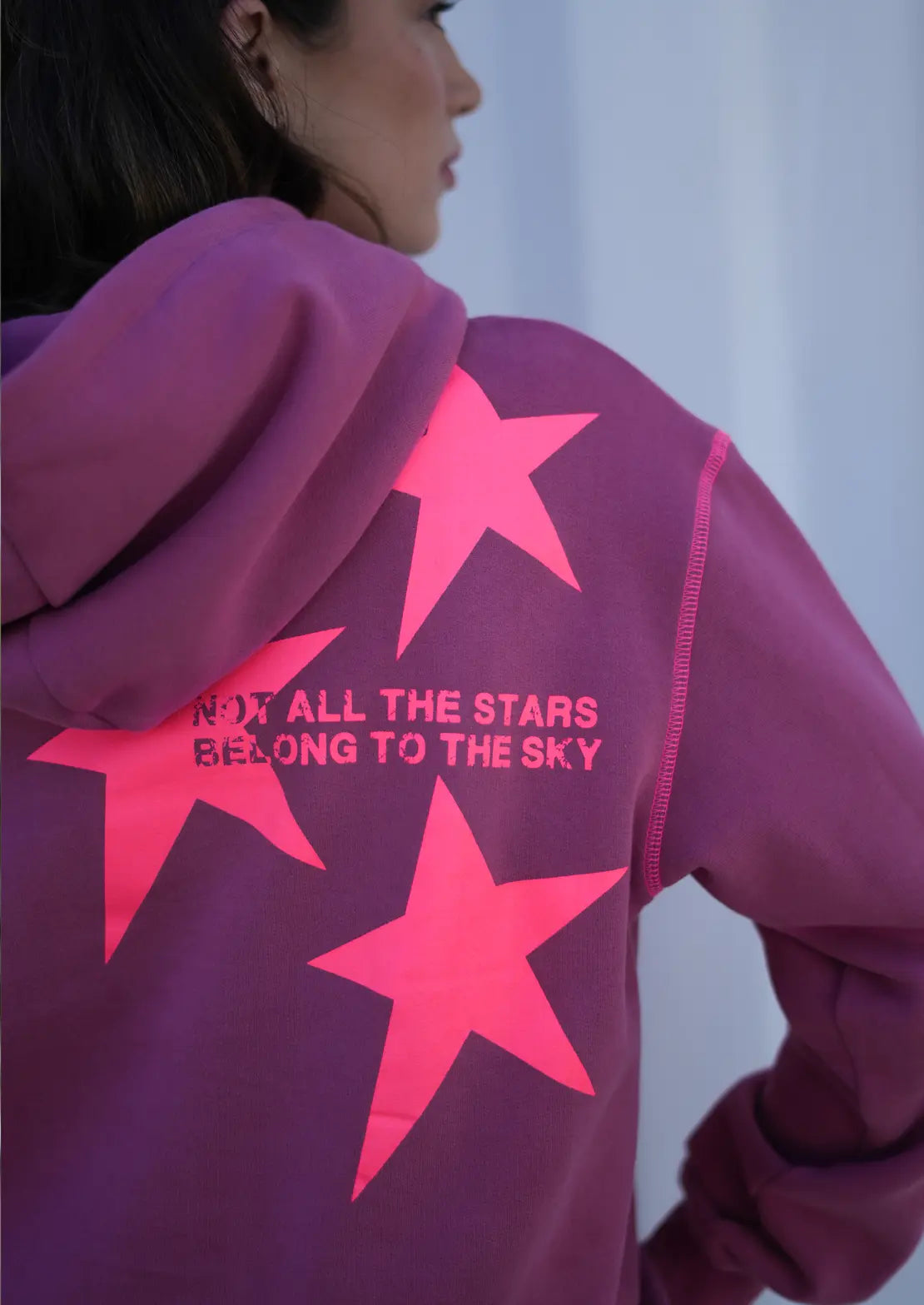 Detalles de Hoodie de To the Moon en color fresa-burdeos con capucha y bolsillo canguro. Estrellas flúor e la espalda.