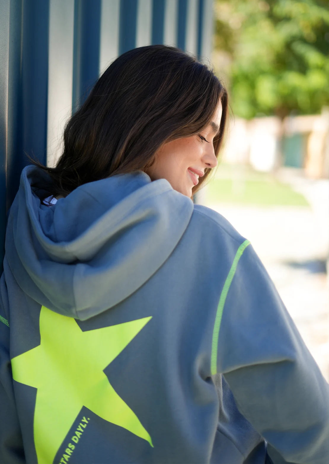 Hoodie de To the Moon en color gris con capucha y bolsillo canguro. Serigrafía trasera amarillo flúor con estrella y frase "Chasing Stars Daily".
