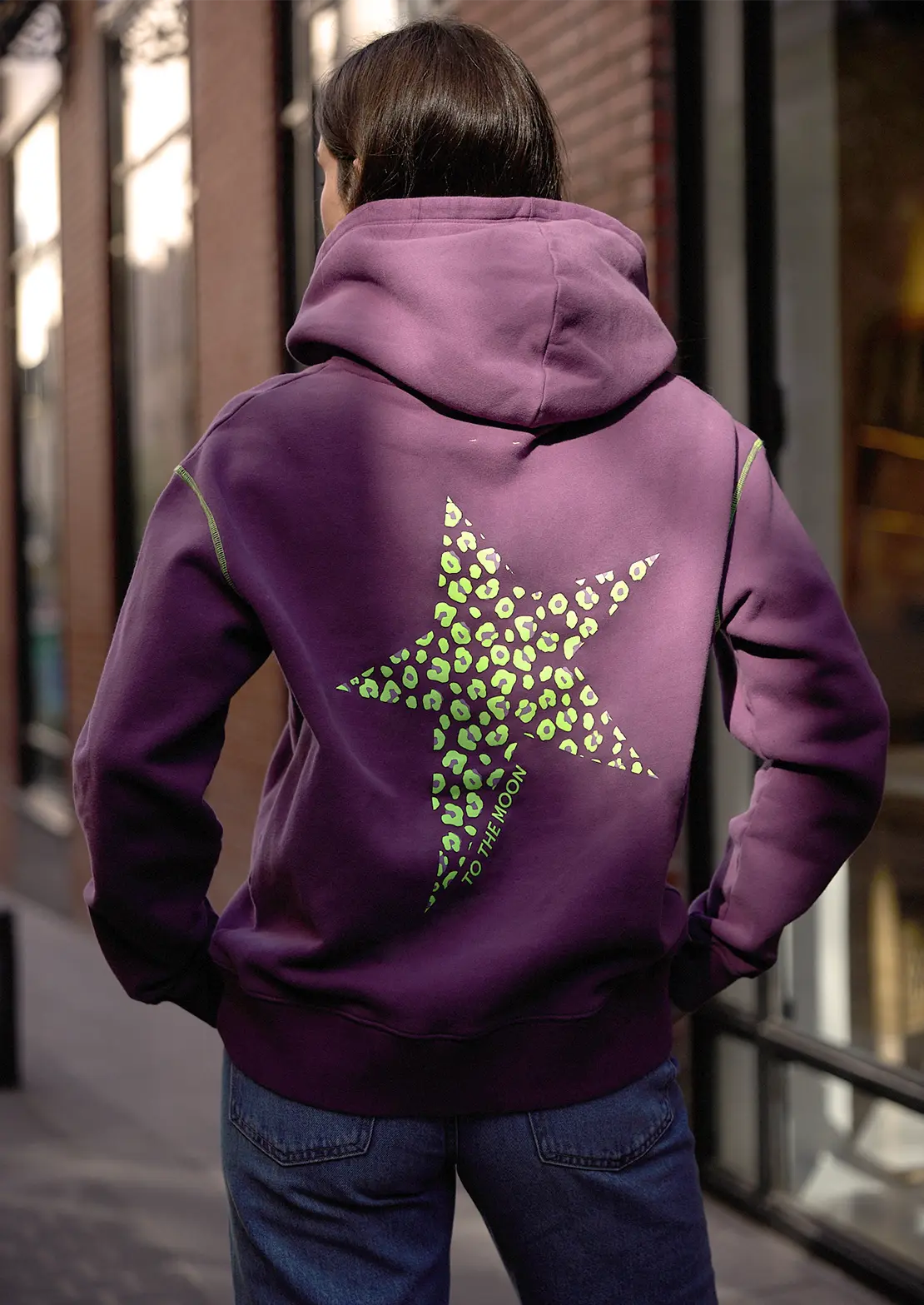 Hoodie de To the Moon en color morado con capucha y bolsillo canguro. Serigrafía amarillo neón en la espalda estrella leopardo.