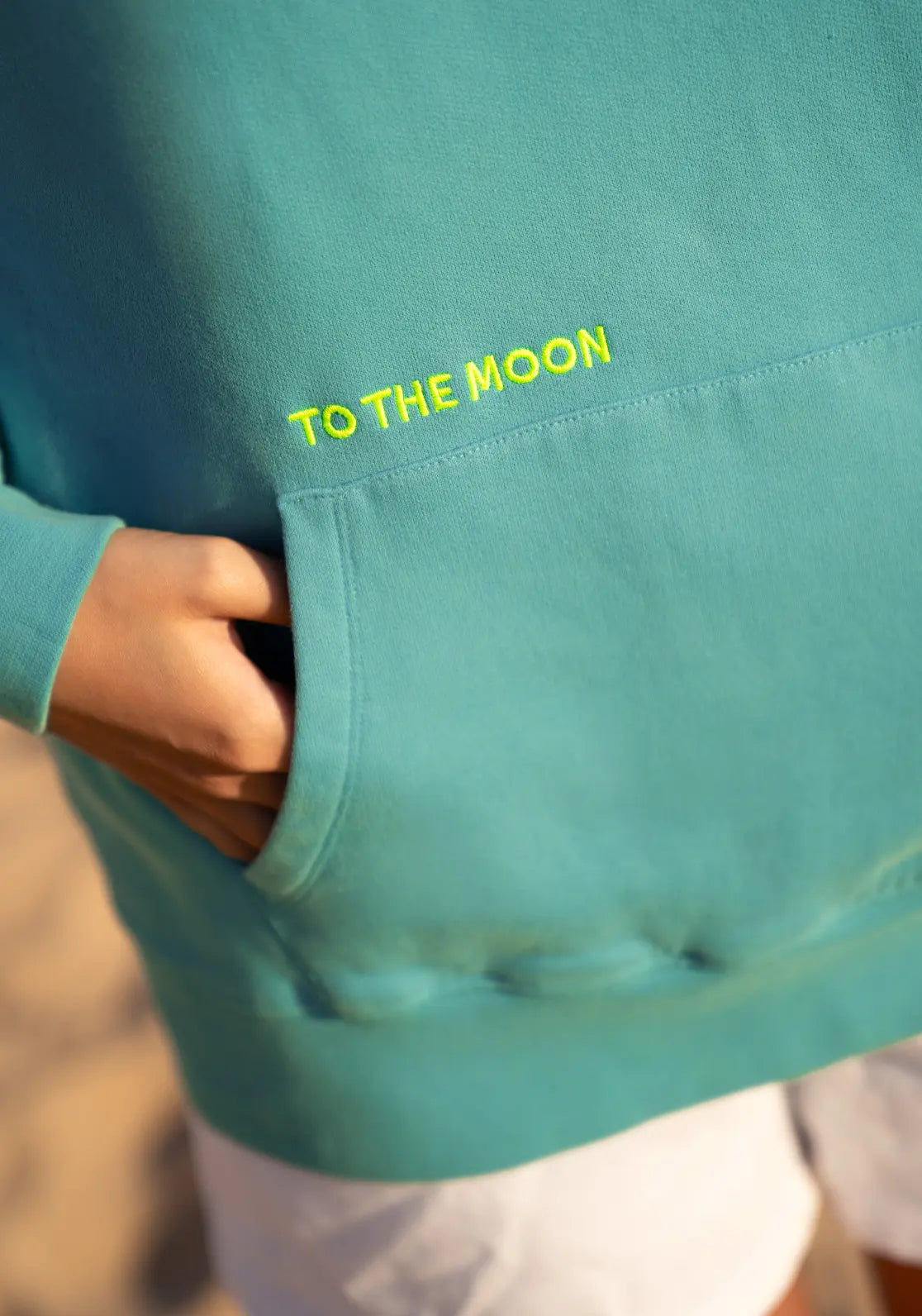 Hoodie Lagoon color verde agua y amarillo flúor. Detalle de bordado sobre bolsillo canguro. 